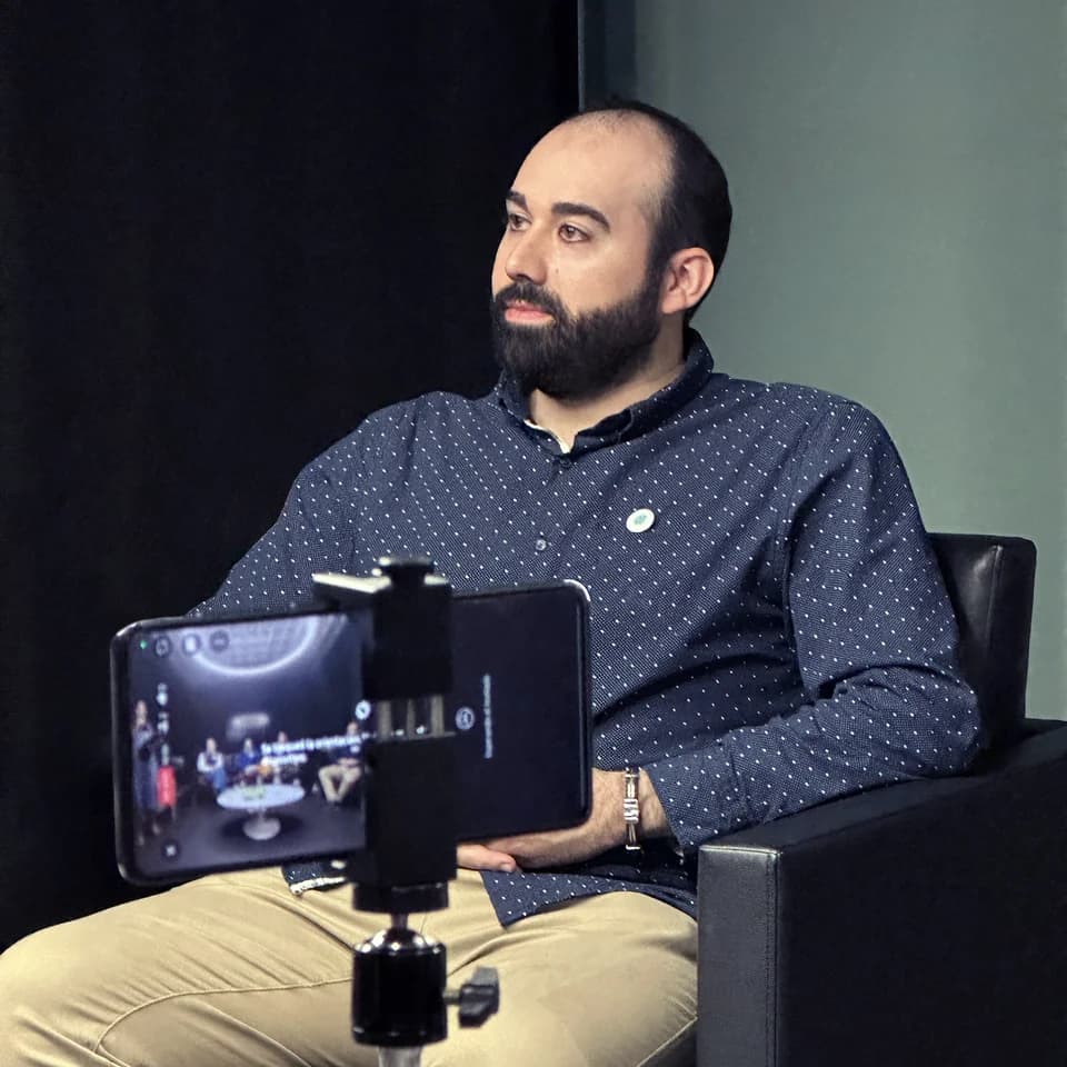 Javier Vicente Molina sentado en una sesión grabando contenido sobre DesignOps con el móvil en trípode, camisa azul oscuro de lunares.